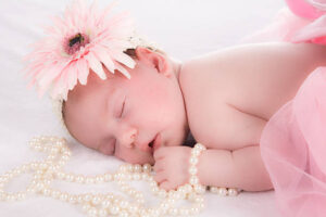 A baby girl with pink tutu and pink flower on her head holding beads and sleeping
